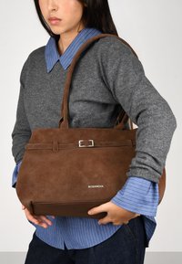 Bolso de mano de ante sintético marrón con forma plana, que presenta un detalle de hebilla plateada y dos asas. Logo "BOSANOVA" grabado en la parte frontal.