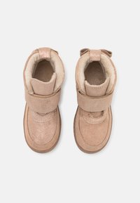 Tan suede boots with a soft interior, featuring a velcro strap, rounded toe, and a decorative bow on the back. Slightly glossy finish.