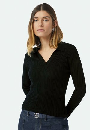 Black ribbed long-sleeve top with a V-neck and flat collar. Features a fitted design and soft texture, paired with dark blue denim jeans.