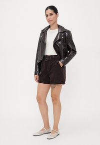 Brown faux leather motorcycle jacket, white fitted shirt, dark brown corduroy shorts, and light gray shoes with mesh accents.
