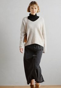 Suéter de punto gris claro con escote en V, superpuesto a un cuello de tortuga negro. Combinado con una larga falda de mezclilla negra y botas de tobillo marrones.