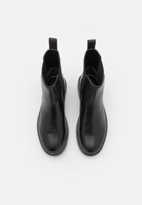 Botas de cuero negras hasta el tobillo con una superficie lisa, paneles laterales elásticos y tiradores en la parte posterior. Punta redonda y suelas de goma planas.