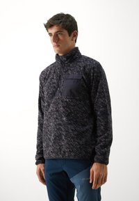 Polarowy sweter w ciemnoszarym kolorze z subtelnym wzorem, z wysokim kołnierzem, zapięciem na guziki oraz kieszenią na piersi z akcentem z ciemnego materiału.
