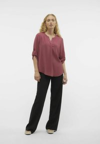 Blusa bordeaux con scollatura a V e maniche arrotolate, abbinata a pantaloni neri a gamba larga. Tessuto morbido e vestibilità rilassata con orlo curvo.