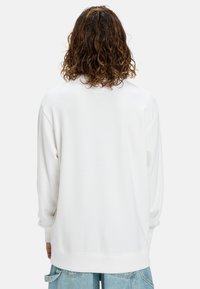 Witte oversized sweatshirt met een ronde hals, lange mouwen en geribde manchetten. Gladde textuur, met een subtiele label op de achterkant.