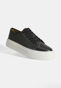 Schwarze Leder-Sneaker mit strukturiertem Obermaterial, glänzendem Kappenzehen und weißer Gummiplattformsohle. Mit sechs schwarzen Ösen und Schnürsenkeln.