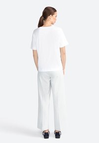 T-shirt bianco a maniche corte abbinato a pantaloni larghi a righe chiare, con vestibilità rilassata e una texture di tessuto morbida. Scarpe nere.