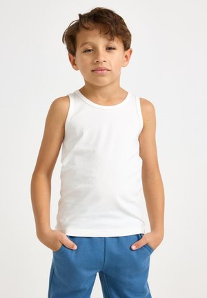Vit bomullstanktopp på ett barn med rund halsringning och avslappnad passform, kombinerad med blå mjukisbyxor. Enkel design utan mönster.