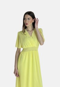 Robe enveloppante jaune avec de courtes manches volantes et une taille smockée. Tissu lisse avec une coupe fluide, atteignant le milieu du mollet. Pas de motifs notables.