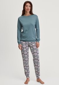 Langsleeve blauwe top gecombineerd met gemusterde pyjamabroek met een bloemmotief in roze, wit en zwart. Zachte stof; elastische boorden bij de enkels.