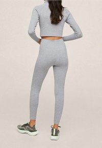 Top corto a coste grigio con maniche lunghe abbinato a leggings grigi a vita alta e scarpe da ginnastica grigie con dettagli verdi. Design semplice.