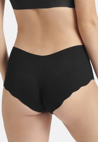Zwarte high-waisted short met een gladde, zachte textuur en een scalloped randontwerp, dat een naadloze pasvorm en minimalistische stijl laat zien.