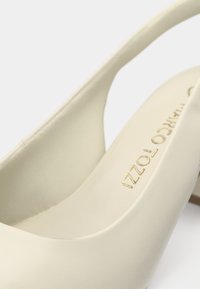 Ελεφαντοστού σλάινγκμπακ παπούτσι από λείο υλικό, με στρογγυλή μύτη, χαμηλό τακούνι και ανάγλυφο λογότυπο στο πέλμα. Μινιμαλιστικός σχεδιασμός με καθαρές γραμμές.