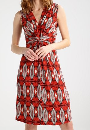 Robe sans manches rouge avec un détail de nœud à la taille, présentant un motif géométrique blanc et noir. Tissu doux et design mi-long.