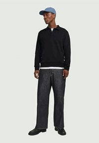 Polo shirt nero a maniche lunghe con colletto, abbinato a jeans di denim scuri e larghi. Un cappellino azzurro chiaro e scarpe nere completano l'outfit.