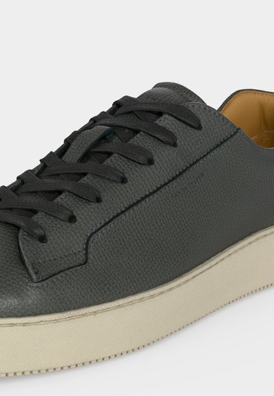 Σκούρο γκρι sneaker από δέρμα με υφή, μαύρα κορδόνια, επενδυμένο γιακά και παχιά λευκοκρεμώδη λαστιχένια σόλα σε απλό φόντο.