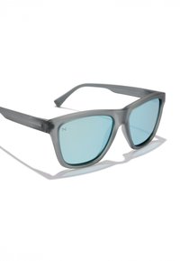 Szürke, matt napszemüveg kékeszöld árnyalatú lencsékkel és szögletes kialakítással. Diszkrét logó található a szárán. Lapos szárai lekerekített élekkel rendelkeznek.