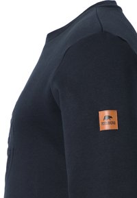 Sudadera azul marino de algodón suave, con cuello redondo y tejido texturizado. Parche de cuero con el logo de un oso en la manga izquierda.
