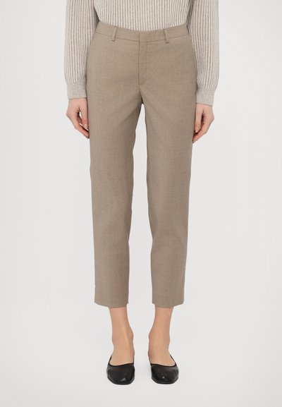 Pantaloni beige su misura con una vestibilità slim, lunghezza cropped e tessuto leggermente texture. Abbinati a scarpe nere basse.