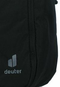 Mochila negra con una tela texturizada, cuenta con una sección con cremallera y muestra un logotipo gris "deuter" en la parte frontal.
