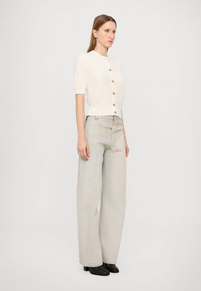 Cream button-up knit top with short sleeves, paired with light gray wide-leg jeans and black ankle boots. Simple, clean design.