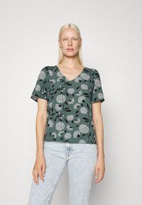 Top verde de mangas curtas com um decote em V, apresentando um padrão floral branco contra um fundo escuro. Tecido texturizado com um corte descontraído.