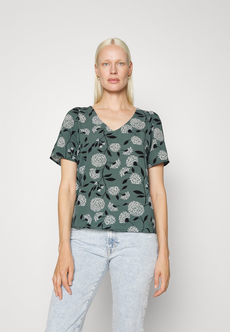 Top verde de mangas curtas com um decote em V, apresentando um padrão floral branco contra um fundo escuro. Tecido texturizado com um corte descontraído.