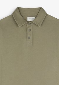 Polo de color verde oliva con collar clásico, tapeta de cinco botones y tejido de algodón suave. Presenta costuras minimalistas y una textura sutil.