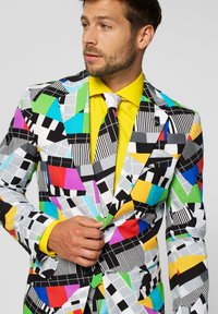 Colorful patterned suit made of fabric featuring geometric shapes in black, white, pink, blue, green, and yellow. Yellow shirt and tie.