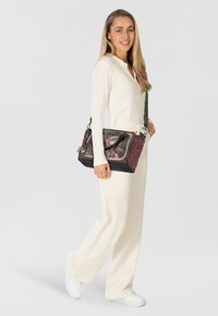 Borsa a spalla nera e bordeaux con motivi floreali, pannello frontale trasparente, accessori in argento e tracolla regolabile.