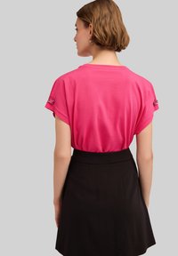 Camiseta de algodón rosa de manga corta y corte holgado, con mangas enrolladas, combinada con una falda negra de talle alto, vista desde la parte de atrás.