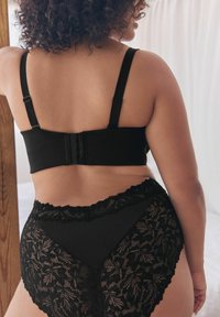 Reggiseno nero con spalline regolabili e chiusura a gancio sul retro, abbinato a mutandine nere a vita alta con motivi floreali in pizzo.