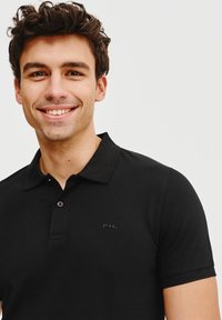 Czarna koszulka polo z teksturowanej tkaniny, z trzema guzikami z przodu i dyskretnym logo na piersi. Krótkie rękawy z eleganckim kołnierzykiem.