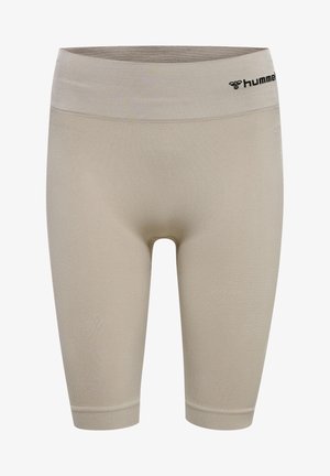 Beżowy top sportowy na ramiączkach i szorty rowerowe, gładka faktura, z logo na pasie i wzorem w zygzak po bokach. Białe trampki.