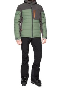 Zelená a šedá zateplená bunda se zipovými kapsami, doplněná černými lyžařskými kalhotami a lyžařskými botami. Bunda má kapuci a kontrastní zipy.