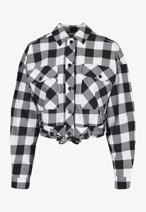 Przycięta czarna i biała koszula w kratkę z długimi rękawami, dwoma przednimi kieszeniami, zapięciem na guziki oraz ściągaczem u dołu. Gładka tekstura materiału.