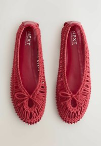 Paire de ballerines tressées rouges avec détail nœud et semelle intérieure en cuir lisse étiquetée Next Forever Comfort sur fond blanc