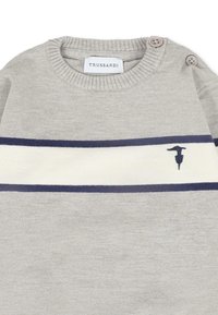 Maglione grigio chiaro con collo rotondo a coste, due bottoni su una spalla e righe orizzontali blu e bianche. Piccolo dettaglio del logo sul petto.