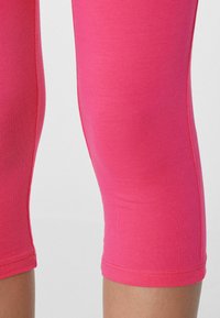 Dámské capri legíny ve jasně růžové barvě, vyrobené z elastického materiálu. Mají hladký povrch a lemované manžety v délce do poloviny lýtek.