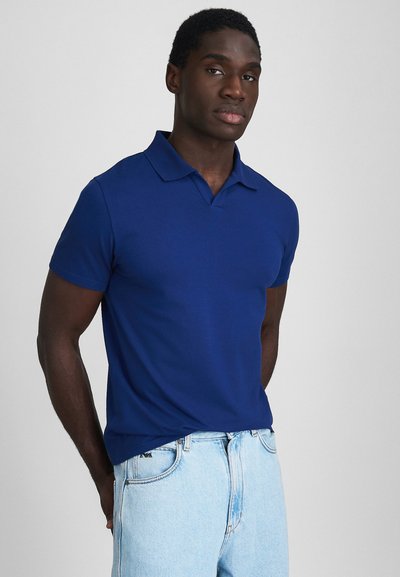 Polo de culoare bleumarin, realizat din bumbac fin, având guler, mâneci scurte și o croială adaptată. Purtați-l cu blugi de culoare albastru deschis.