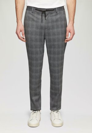 Pantalons à carreaux gris avec une taille à cordon, présentant un tissu texturé et de subtils accents bleus, associés à des baskets blanches.