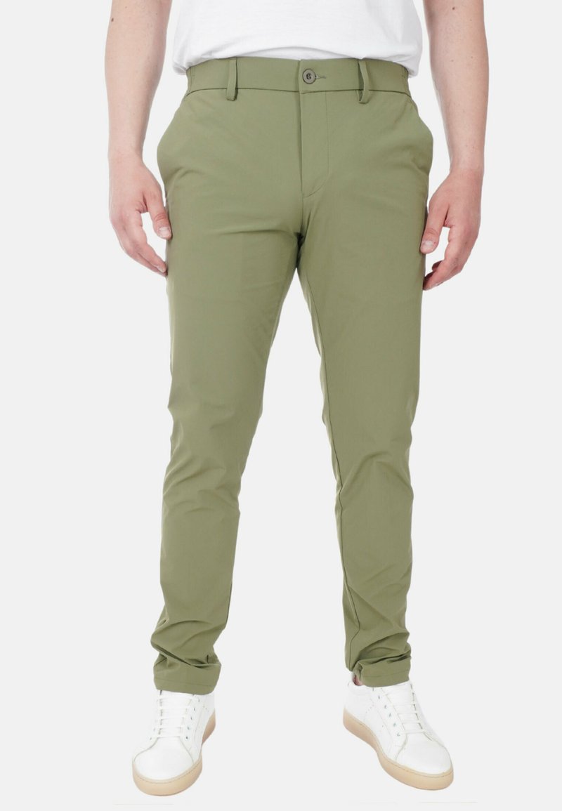 Pantaloni su misura verde oliva realizzati in tessuto leggero, con fronte piatto, passanti per cintura e chiusura con un bottone. Indossati con sneakers bianche.