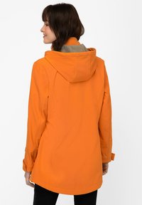 Oranssi vedenpitävä takki hupulla, jossa on beige sisävuori. Silkkinen pinta, hieman ylipitkä muotoilu ja säädettävät hihansuut.