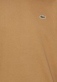 Camiseta de manga corta de tela suave y acanalada que presenta un pequeño logo de cocodrilo verde con detalles rojos en el lado izquierdo.