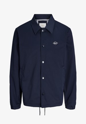 Veste légère bleu marine avec col, boutons-pression métalliques, poignets élastiques, poches latérales et petit logo en forme de diamant sur la poitrine.