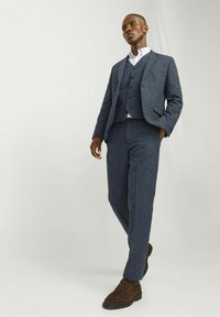 Marineblauer dreiteiliger Anzug aus strukturiertem Stoff. Taillierte Jacke, Weste und Hose mit einem dezenten Muster. Braune Schuhe runden den Look ab.