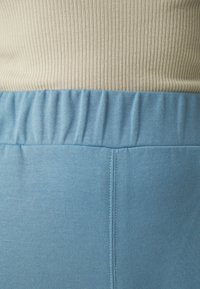 Zils elastīgs jostasviets ar ribotu tekstūru augšpusē un gludu audumu apakšpusē, ar tīru šuvumu sānos.