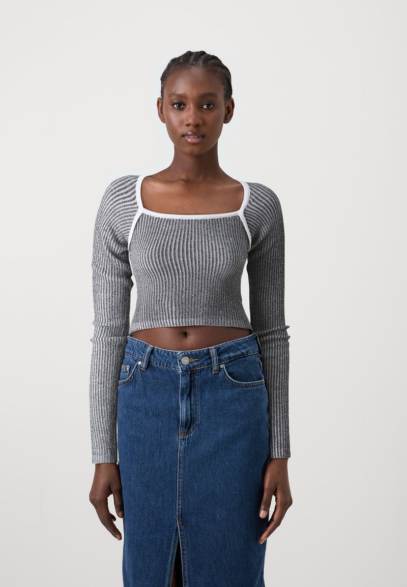 Szürke bordázott crop top hosszú ujjakkal és fehér díszítéssel, magas derekú farmer szoknyával párosítva, amely elől hasítással és gombos zárással rendelkezik.