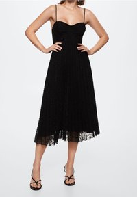 Černé krajkové midi šaty se zavazováním přes ramena, přiléhavým trupem, rozšířenou sukní a texturovaným květinovým vzorem. Doplněné černými sandály na řemínky.