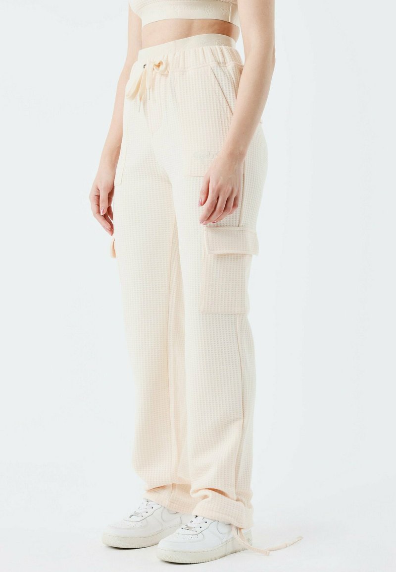 Pantalons cargo en tissu gaufré, beige clair, avec une taille élastique et un cordon de serrage. Comprend des poches latérales et des poignets côtelés.